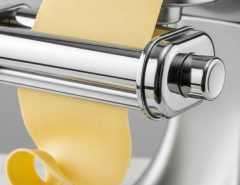 Close-up of stainless steel pasta roller attaching to stand mixer with smooth dough sheet emerging