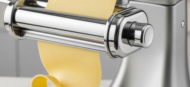 Close-up of stainless steel pasta roller attaching to stand mixer with smooth dough sheet emerging
