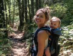Happy mom hiking with baby in ergonomic carrier on sunny trail
