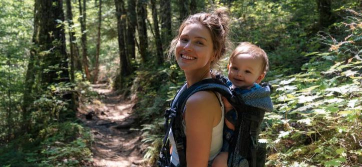 Happy mom hiking with baby in ergonomic carrier on sunny trail