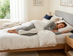 Side sleeper relaxing in bed with an ergonomic knee pillow.