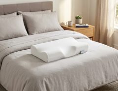 Ergonomic cervical memory foam pillow resting on a modern neutral bed.