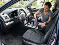 Person using a portable vacuum to clean a car seat crevice.
