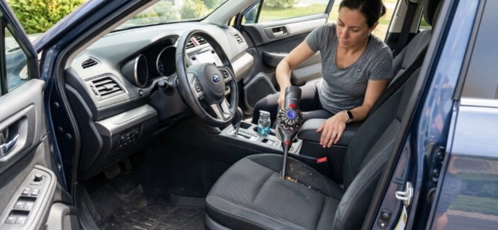 Person using a portable vacuum to clean a car seat crevice.